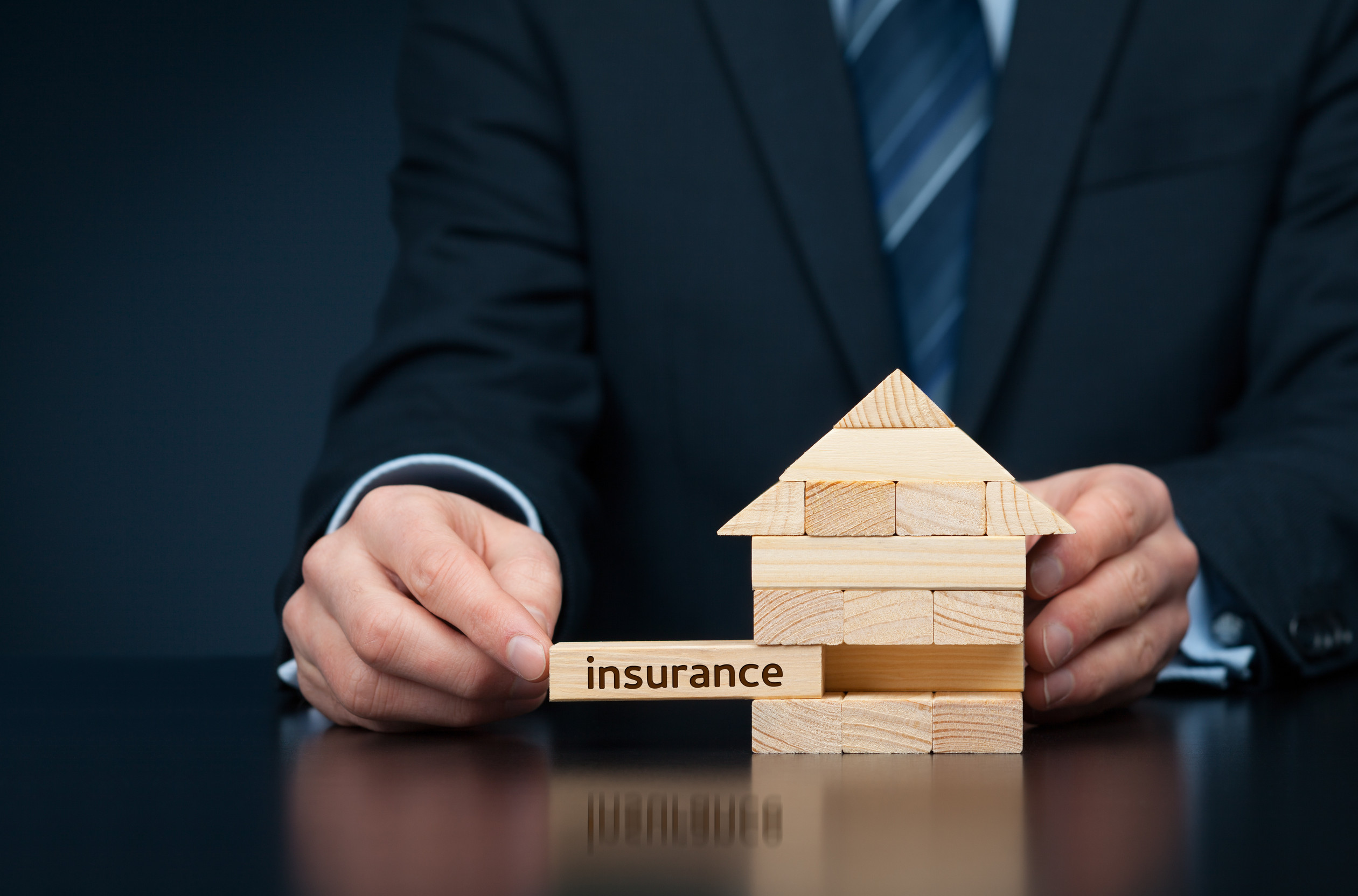 Property (family house) insurance protection concept. Insurance agent complete wooden model of the house with last piece with text insurance.